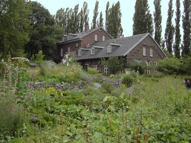 Naturschutzzentrum Bruchhausen in Erkrath Ein historisches Backsteingebäude umgeben von einer üppigen, vielfältigen Gartenlandschaft im Naturschutzgebiet.