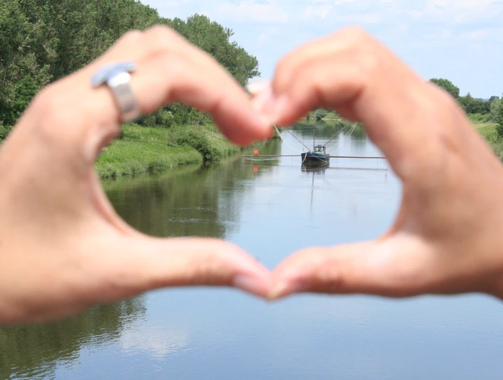 Hände formen Herz und rahmen einen traditionellen Aalschokker auf einem ruhigen Fluss ein.Hands form hearts and frame a traditional eel barge on a calm river.Hænder danner hjerter og indrammer en traditionel ålepram på en rolig flod.Handen vormen harten en omlijsten een traditionele palingschuit op een kalme rivier.