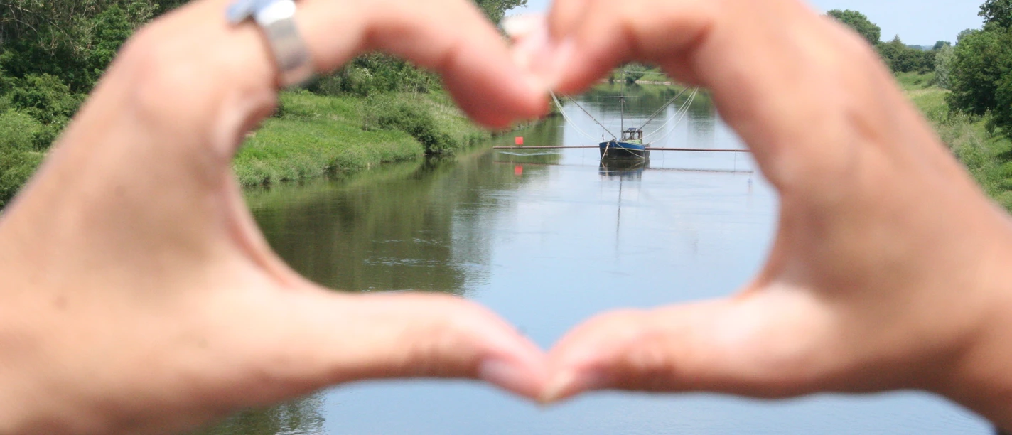 Aalschokker Weser Hands form hearts and frame a traditional eel barge on a calm river.