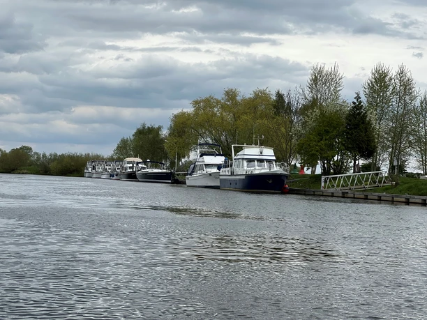 Verdener Motorbootverein Am Flussufer liegen mehrere Motorboote vertäut, umgeben von Bäumen und unter einem bewölkten Himmel.