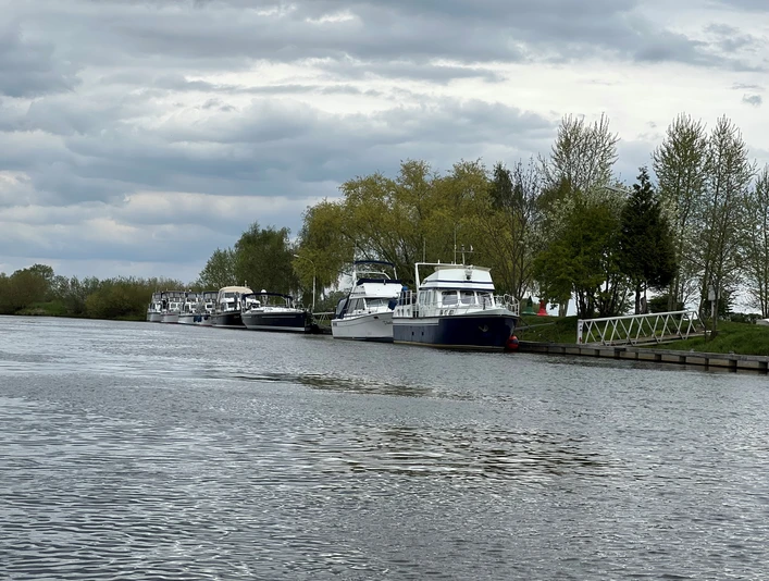 Verdener Motorbootverein Am Flussufer liegen mehrere Motorboote vertäut, umgeben von Bäumen und unter einem bewölkten Himmel.