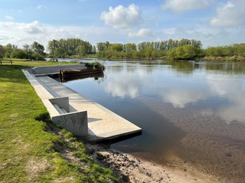 Wassersportverein Verden Bootsanleger aus Beton führt zum ruhigen Flussufer mit grüner Landschaft und bewölktem Himmel im Hintergrund.