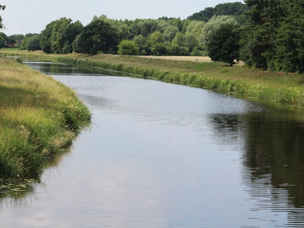 A calm river course through a green, tree-lined landscape under a clear sky.