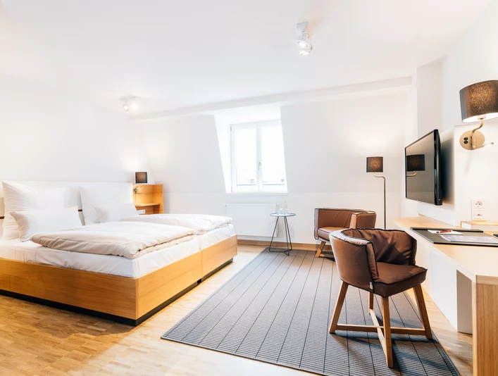 Liborianum, Zimmer Helles, modernes Hotelzimmer mit Doppelbett, Schreibtisch, Stuhl und Wandfernseher in stilvollem Design.