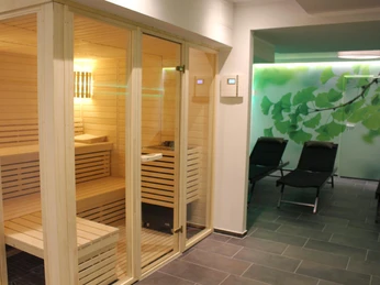 Moderne Sauna mit hölzerner Verkleidung, Ruheliegen und einem dekorativen Blattmotiv an der Wand.