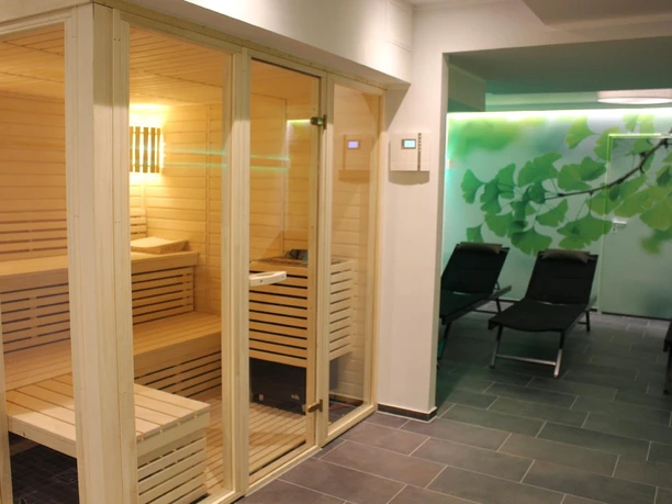 Moderne Sauna mit hölzerner Verkleidung, Ruheliegen und einem dekorativen Blattmotiv an der Wand.