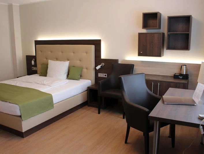 Modern eingerichtetes Hotelzimmer mit Doppelbett, Schreibtisch, Stühlen und Holzregalen an der Wand.