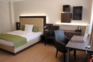 Landhaus Jägerkrug - Zimmer Modern eingerichtetes Hotelzimmer mit Doppelbett, Schreibtisch, Stühlen und Holzregalen an der Wand.