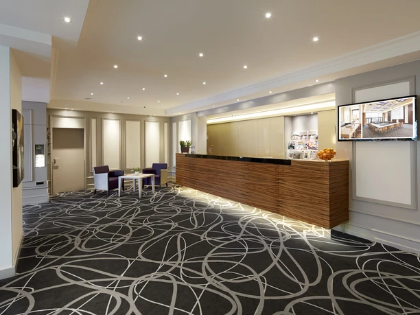 Moderne Hotellobby mit großem Empfangstresen, gemütlichen Sitzgelegenheiten und heller Beleuchtung.