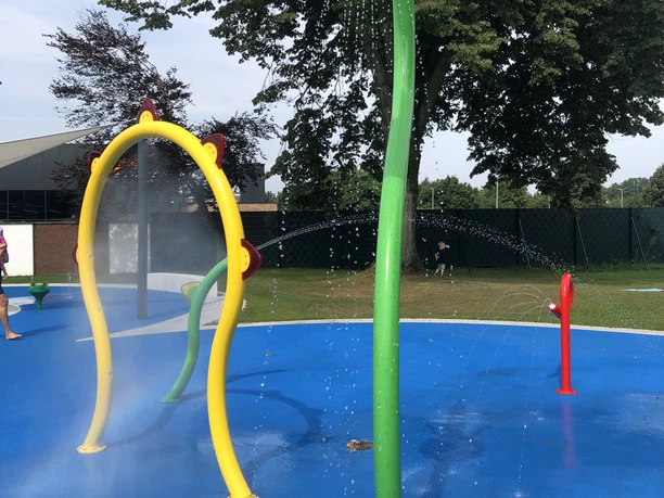 Bunt gestalteter Wasserspielplatz mit sprühenden Wasserfontänen in tierischer Form auf blauem Boden.