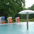Harsewinkeler Freibad mit Strandkörbe am Kinderbecken Ein ruhiges Schwimmbad mit einem Wassersprühpilz und bunten Strandkörben vor grüner Kulisse.