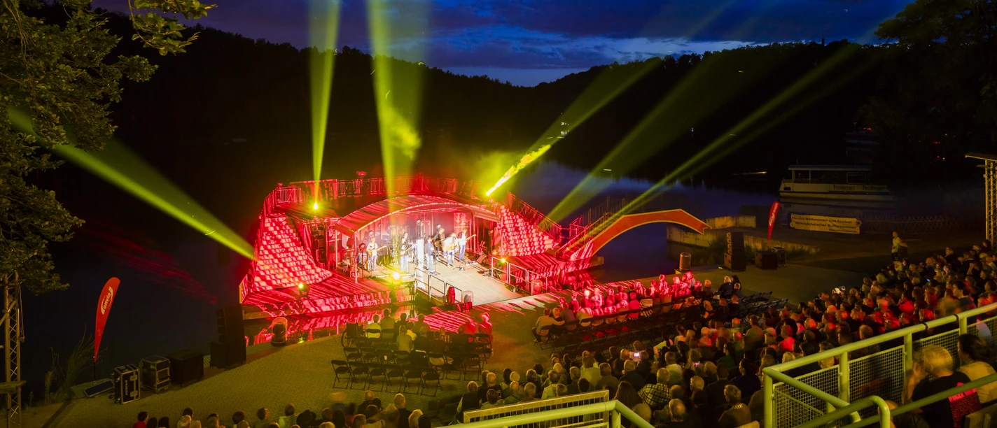 Seebühne Kriebstein - Culture à Leipzig et dans la région La vue sur la Seebühne Kriebstein depuis les gradins supérieurs, un concert est joué, les places des spectateurs sont remplies et les projecteurs brillent dans les différentes directions à l'heure bleue, culture, manifestation
