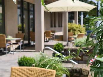 Terrasse des Hotel Aspethera mit Rattanmöbeln, umgeben von grünen Pflanzen und Sonnenschirmen.