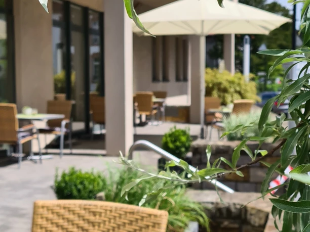 Terrasse des Hotel Aspethera mit Rattanmöbeln, umgeben von grünen Pflanzen und Sonnenschirmen.