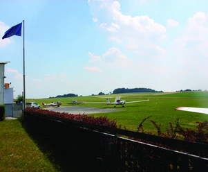 Segelflugplatz Meiersberg in Heiligenhaus Segelflugzeuge stehen auf einem weitläufigen, grünen Flugfeld unter einem blauen Himmel.