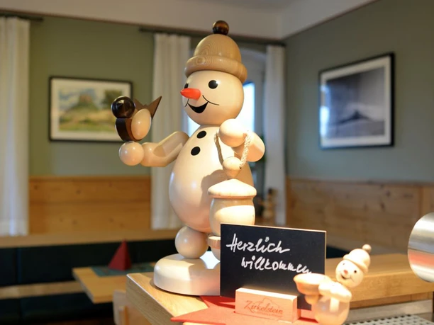 Wooden figure of a smiling snowman with bird and lantern, next to a sign saying "Welcome" in a cozy room.