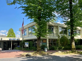 tourist-information-bad-zwischenahn-aussen.jpg Tourist-Information Bad Zwischenahn mit barrierefreiem Zugang und Beschilderung, umgeben von grünen Bäumen.