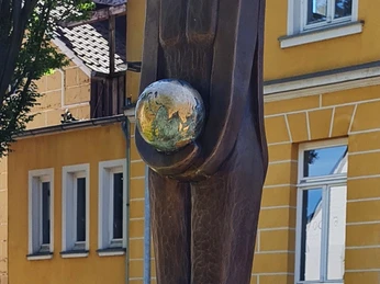 Vlothoer WächterIn.jpg Bronzestatue in Vlotho, die eine stehende Figur mit einem Erdball in den Händen darstellt.