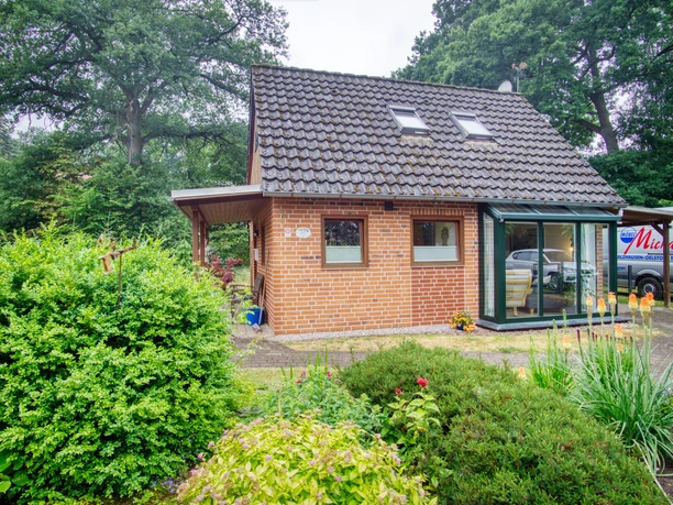Außen-total.jpg Rotes Backstein-Ferienhaus mit Wintergarten und Ziegeldach inmitten eines grünen Gartens.