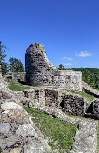 Ruinen der Falkenburg mit erhaltenem Turmstumpf im Hintergrund, umgeben von grünen Wäldern.