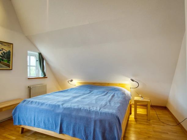 Schlazimmer 1 Helles Schlafzimmer mit Dachschräge, Holzboden und Doppelbett mit blauer Decke.