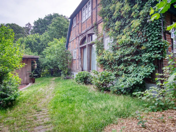 Aussenansicht-patze.jpeg Rotes Fachwerkhaus mit efeubewachsener Fassade, großen Fenstern und einem grünen Gartenweg.