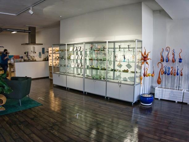 Verkaufsraum Heller Verkaufsraum mit Vitrinen voller Glaskunst, dunklem Holzboden und buntem Glasschmuck.