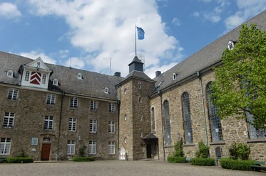 Schloss Hückeswagen Schloss Hückeswagen mit historischem Mauerwerk und Turm unter blauem Himmel, umgeben von Bäumen.