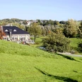 Golf Club Grevenmühle in Ratingen Ein modernes Clubhaus liegt eingebettet in eine weitläufige, grüne Parklandschaft mit vereinzelten Bäumen.