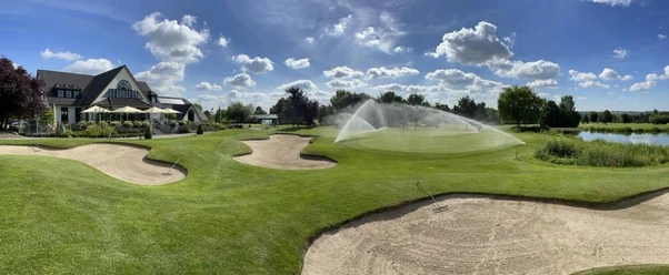 Golfclub Haan-Düsseltal Eine gepflegte Rasenfläche mit Sandbunkern, im Hintergrund ein Clubhaus und ein Wasserhindernis.