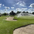 Golfclub Haan-Düsseltal Eine gepflegte Rasenfläche mit Sandbunkern, im Hintergrund ein Clubhaus und ein Wasserhindernis.