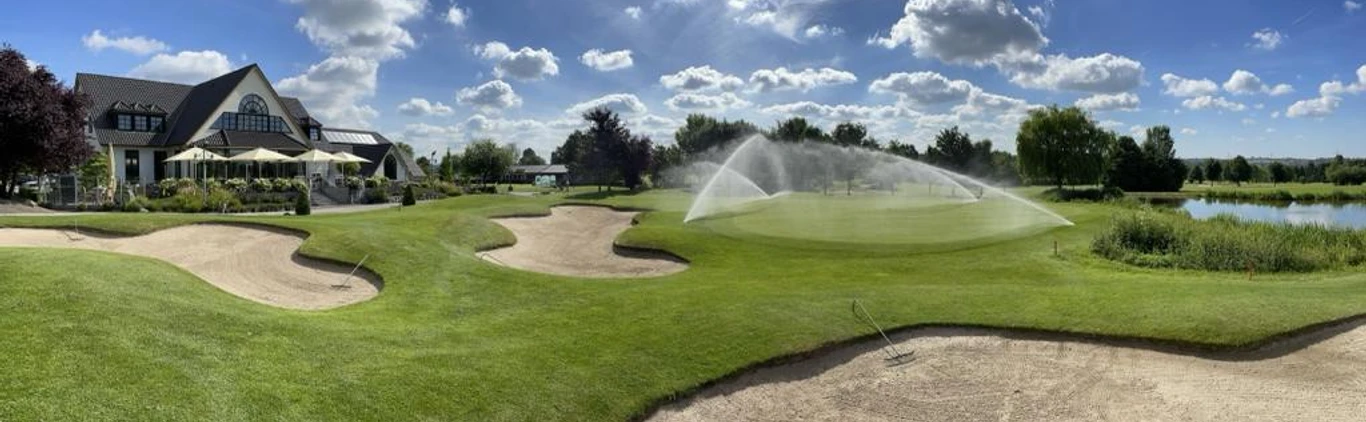 Golfclub Haan-Düsseltal Eine gepflegte Rasenfläche mit Sandbunkern, im Hintergrund ein Clubhaus und ein Wasserhindernis.