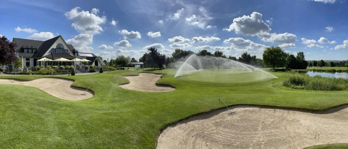 Golfclub Haan-Düsseltal Eine gepflegte Rasenfläche mit Sandbunkern, im Hintergrund ein Clubhaus und ein Wasserhindernis.