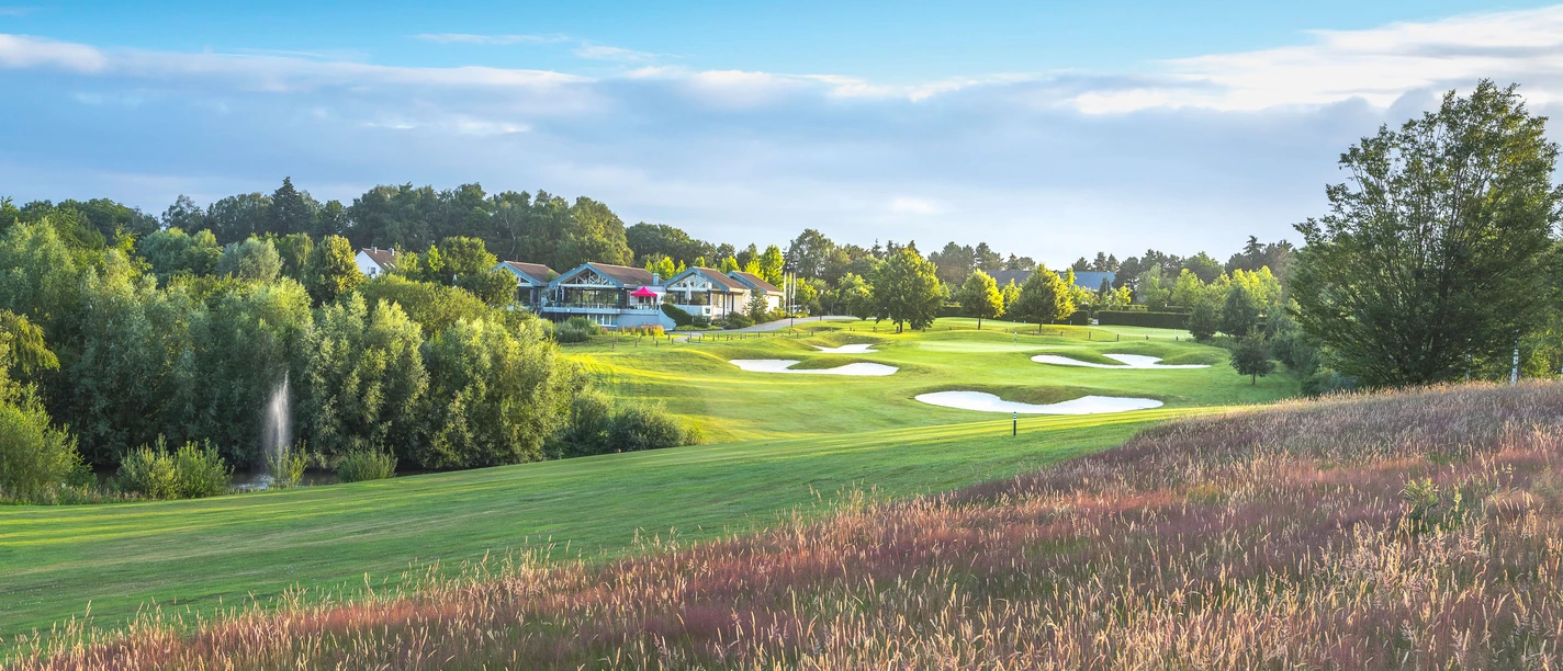 Golfclub Hösel in Heiligenhaus Golfplatz mit gepflegtem Grün und Bunkern, umgeben von Bäumen und einem Clubhaus im Hintergrund.