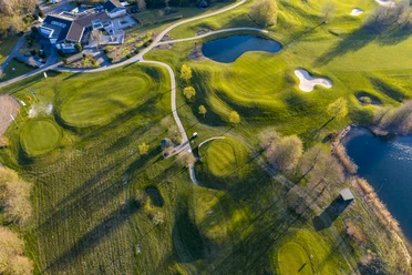 Golfclub Mettmann e.V. Luftaufnahme eines Golfplatzes mit grünen Fairways, Seen, Sandbunkern und angrenzendem Klubhaus.