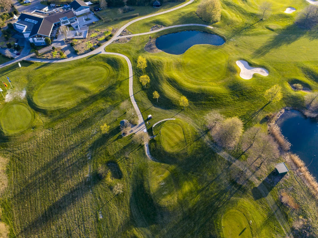 Golfclub Mettmann e.V. Luftaufnahme eines Golfplatzes mit grünen Fairways, Seen, Sandbunkern und angrenzendem Klubhaus.
