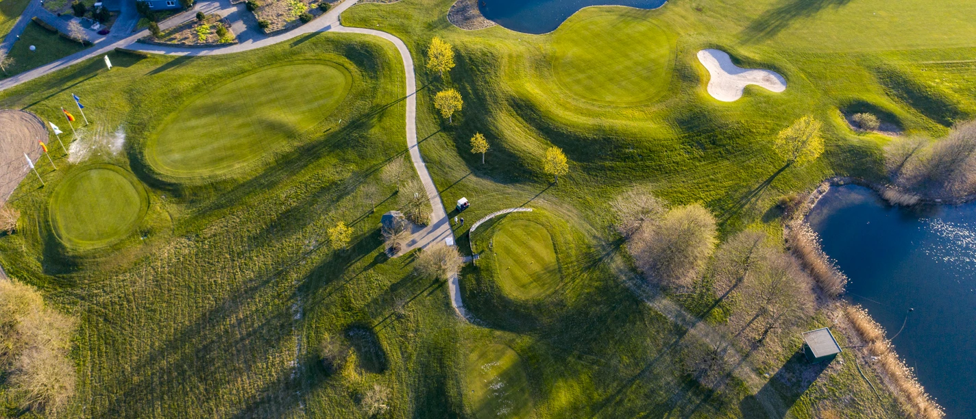 Golfclub Mettmann e.V. Luftaufnahme eines Golfplatzes mit grünen Fairways, Seen, Sandbunkern und angrenzendem Klubhaus.
