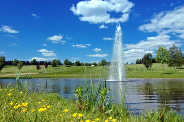 GC Velbert Ein gepflegter Golfplatz mit sauberem Gewässer und sprudelndem Springbrunnen unter blauem Himmel.