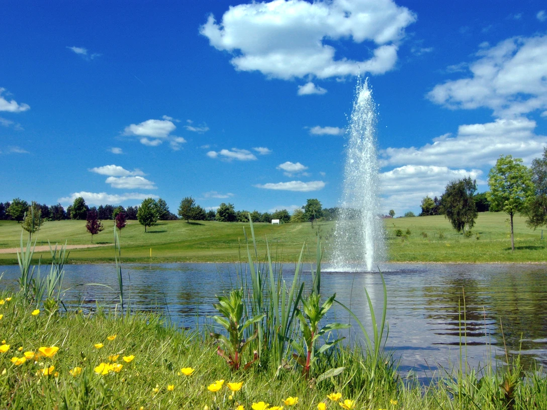 GC Velbert Ein gepflegter Golfplatz mit sauberem Gewässer und sprudelndem Springbrunnen unter blauem Himmel.