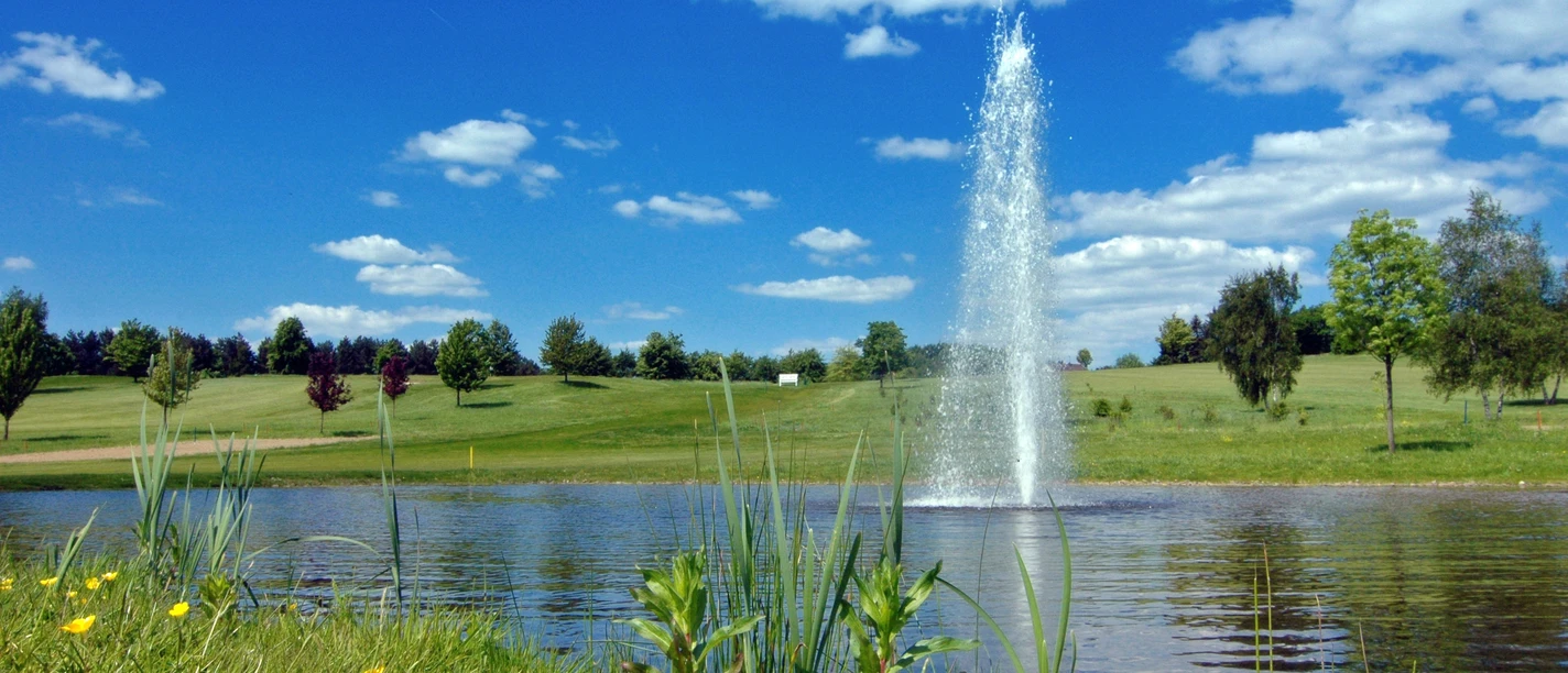 GC Velbert Ein gepflegter Golfplatz mit sauberem Gewässer und sprudelndem Springbrunnen unter blauem Himmel.