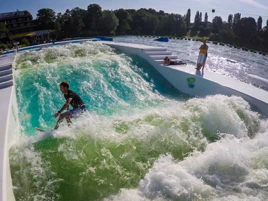 Surfing bei Wasserski Langenfeld Ein Surfer balanciert mit ausgebreiteten Armen auf einer künstlichen stehenden Welle im Park.