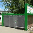 Grüne Mobilstation am Bahnhof mit Fahrradständern und überdachten Sitzmöglichkeiten vor Bäumen.