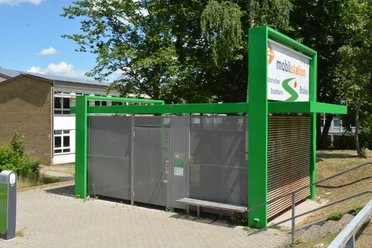 Mobilstation am Bahnhof Grüne Mobilstation am Bahnhof mit Fahrradständern und überdachten Sitzmöglichkeiten vor Bäumen.