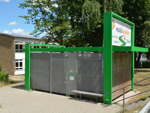 Mobilstation am Bahnhof Grüne Mobilstation am Bahnhof mit Fahrradständern und überdachten Sitzmöglichkeiten vor Bäumen.