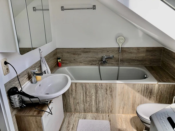 Helles Badezimmer mit Dachschräge, freistehender Badewanne, Waschbecken und Spiegelwand.