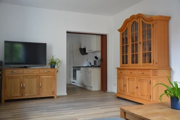 Gasthof zum Herzog Wohnzimmer mit Holzmöbeln und Blick in eine moderne Küche; heller Holzfußboden, Pflanzen im Raum.