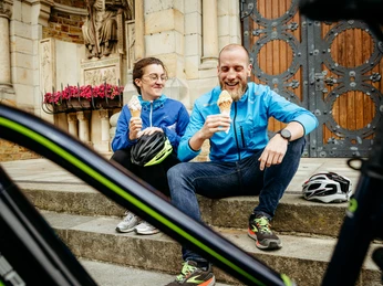 Radfahren auf der Artland-Rad-Tour Zwei Personen in blauen Jacken genießen Eis auf Treppenstufen. Fahrräder im Vordergrund.Two people in blue jackets enjoying ice cream on steps. Bicycles in the foreground.To personer i blå jakker nyder en is på en trappe. Cykler i forgrunden.Twee mensen in blauwe jassen genieten van een ijsje op een trapje. Fietsen op de voorgrond.