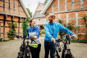Radfahren auf der Artland-Rad-Tour Lachend stel met fietsen voor historische vakwerkhuizen in een landelijke omgeving.