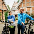 Radfahren auf der Artland-Rad-Tour Lächelndes Paar mit Fahrrädern vor historischen Fachwerkgebäuden in ländlicher Umgebung.Smiling couple with bicycles in front of historic half-timbered buildings in a rural setting.Smilende par med cykler foran historiske bindingsværksbygninger i landlige omgivelser.Lachend stel met fietsen voor historische vakwerkhuizen in een landelijke omgeving.