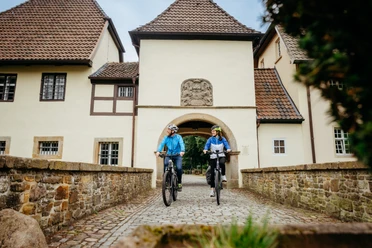 An der Klosterpforte in Bersenbrück Twee fietsers passeren een historisch poortgebouw op kasseien.